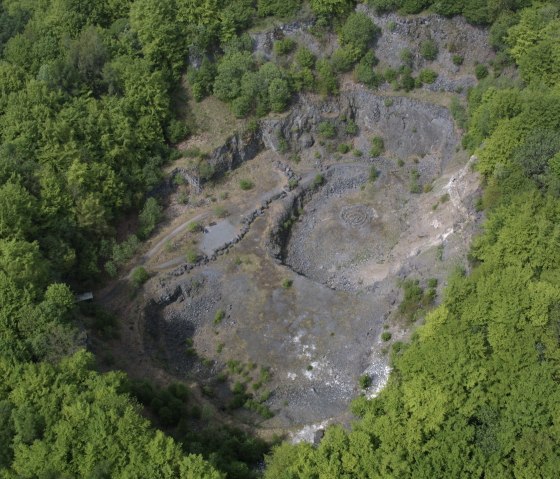 Luchtfoto van de beboste krater van de vulkaan Arensberg met stenige gebieden en omringend dicht bos., © Regnery