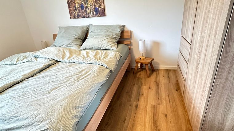 Ein gemütliches Schlafzimmer mit einem Doppelbett und Holzfußboden. An der Wand hängt ein Bild von einer gelben Blumenwiese.