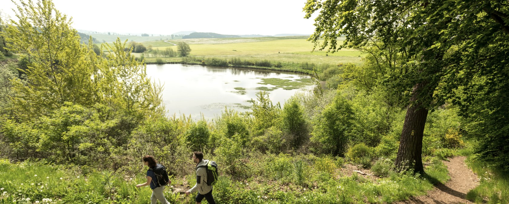 Twee wandelaars op een pad naast een meer in een groen landschap.