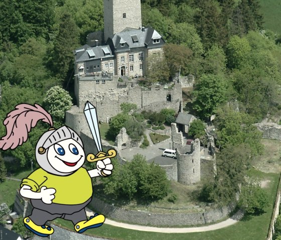 Stripfiguur Willi Basalt met een groen shirt, grijze broek, gele schoenen, een ridderhelm op zijn hoofd en een zwaard in zijn hand. Achter hem is een luchtfoto van Kasteel Kerpen te zien.