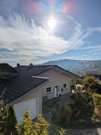 Une maison moderne avec un jardin soigné et une vue pittoresque sur les montagnes. Le ciel est clair et le soleil brille fortement.