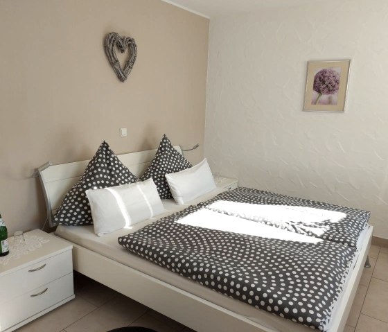 Ein minimal eingerichtetes Schlafzimmer mit einem großen bezogenen Doppelbett mit Nachttischen daneben und einem Bild an der Wand.