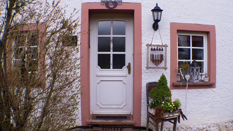 Een uitnodigende voordeur met een witte omlijsting en roze accenten. Naast de deur staan planten en een decoratieve lantaarn die een gezellige sfeer creëert.