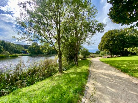 Ein Weg führt an einem Teich vorbei, umgeben von Bäumen und Gras im Bolsdorfer Tälchen.