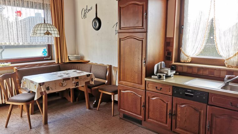 A cozy kitchen with wooden furniture and a dining area. The window is decorated with curtains and brings natural light in.