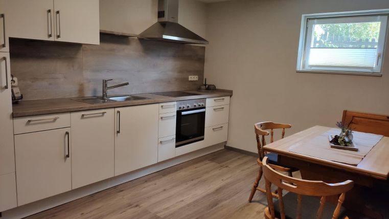 Une cuisine moderne avec des armoires blanches et une cuisinière. Une table à manger avec des chaises en bois se trouve dans le coin.