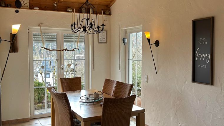 Une salle à manger lumineuse avec une grande table en bois et des chaises élégantes. Le mur est décoré avec un éclairage moderne et des décorations.