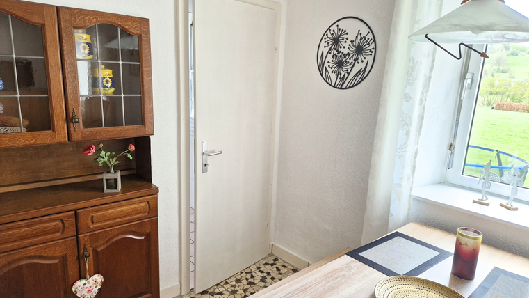 Une cuisine confortable avec un placard en bois et une table. À travers la fenêtre, on peut voir un jardin avec des espaces verts.