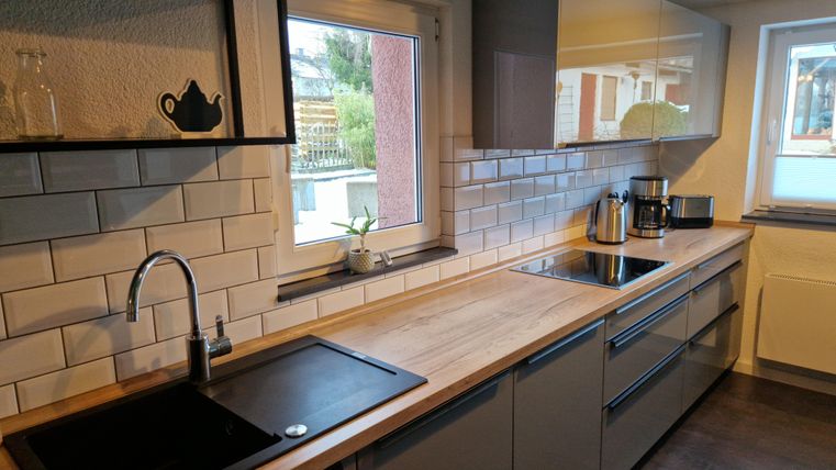 Eine moderne Küche mit Holzarbeitsplatte und eleganten grauen Schränken. Große Fenster sorgen für viel natürliches Licht.