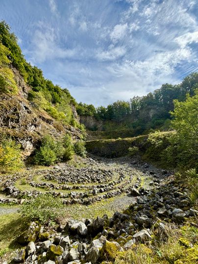 Stone spiral in the Arensberg volcano with wooded rock faces and blue sky.
