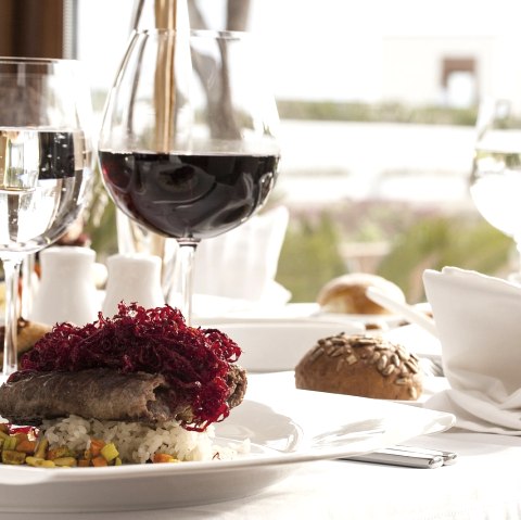 Ansehnlich dekorierter Tisch eines Restaurants mit verschiedenen Speisen auf den Tellern und Wein- und Wassergläsern daneben.