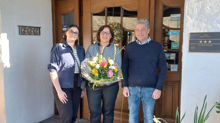 Drei Personen halten einen Blumestrauß vor der Eingangstür des Landhauses.