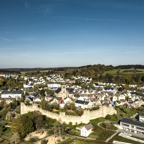 Luftaufnahme von Hillesheim: Historische Stadtmauer, Kirche und moderne Geb&auml;ude inmitten gr&uuml;ner Landschaft unter blauem Himmel., &copy; Eifel Tourismus GmbH, Dominik Ketz