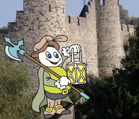 Cartoonfigur Willi Basalt mit grünem Shirt mit Umhang, grauer Hose und Stiefeln ist verkleidet als Nachtwächter mit Lampe und Axt. Hinter ihm eine Fotoaufnhame der Stadtmauer von Hillesheim.
