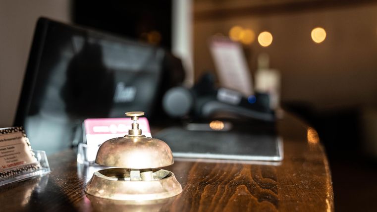A reception desk with a classic hotel bell. In the background, the controls and information are visible.