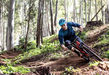 A man dressed in sportswear and wearing a helmet rides through a forest on a steep slope.