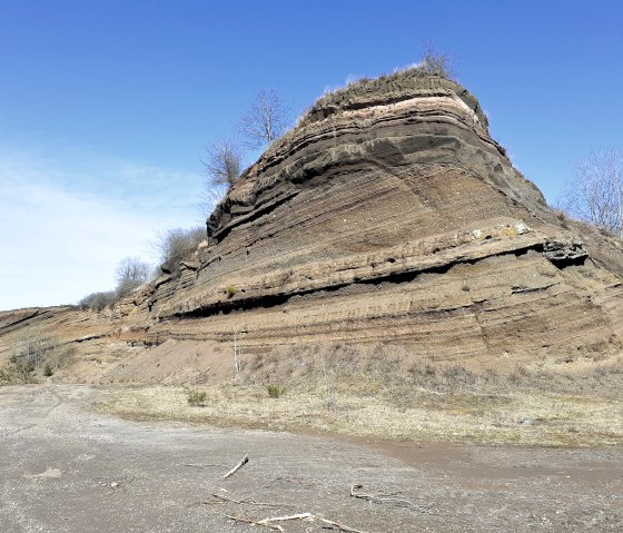 Rock layers on the Rockeskyller Kopf, showing the geological structure. The sky is clear and blue, some trees are visible., © Touristik GmbH Gerolsteiner Land, Ute Klinkhammer