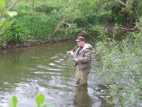 Mann steht in der Kyll mit einer Angel in der Hand