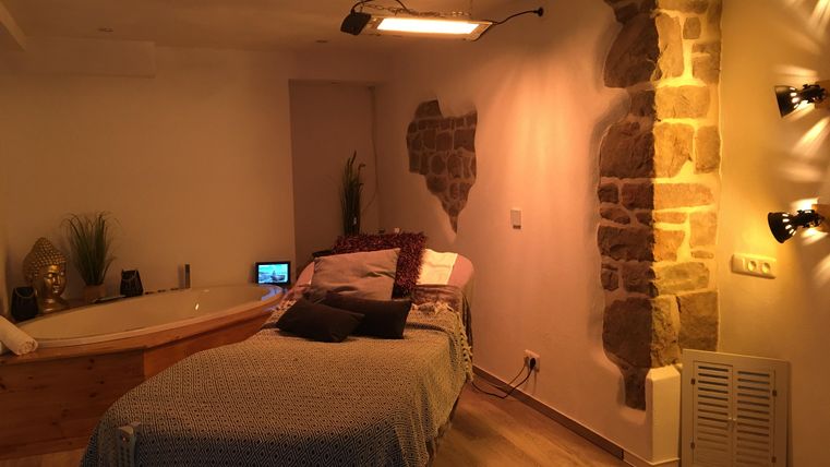 Une salle de bien-être confortable avec un lit de massage et une baignoire. Les murs sont partiellement en pierre et l'éclairage crée une atmosphère détendue.