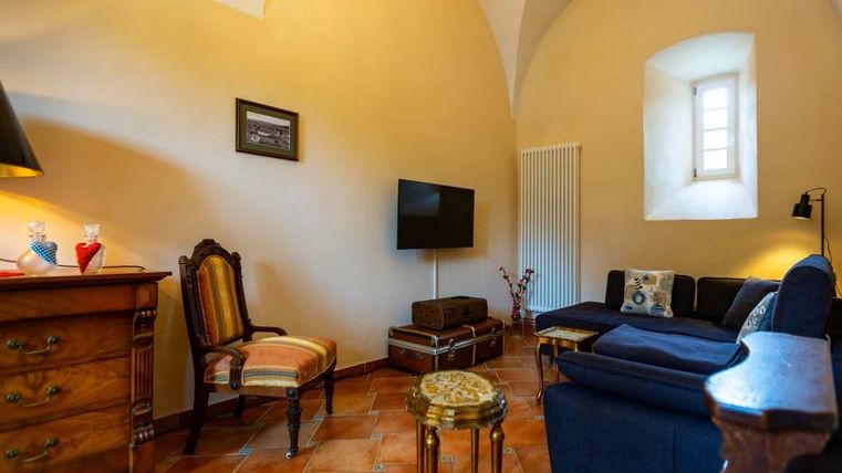 Ein gemütlicher Wohnraum mit hohen Decken und einem großen Fenster. Zu sehen sind ein Sofa, ein Fernseher und einige dekorative Möbelstücke.