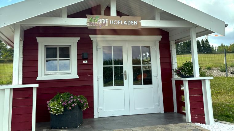 Ein rotes Holzhaus mit einem weißen Dach und einer einladenden Eingangstür. Vor dem Haus stehen Pflanzen in Töpfen und der Bereich ist gepflegt.