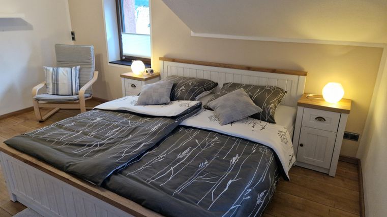 Ein gemütliches Schlafzimmer mit einem großen Doppelbett und modernen Kissen. Ein Stuhl und sanfte Beleuchtung schaffen eine einladende Atmosphäre.