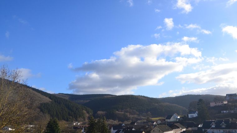 Een schilderachtig dorp in de bergen, omgeven door bosrijke heuvels. De lucht is helder met enkele wolken.