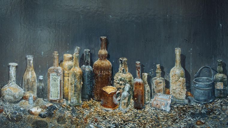 Eine Sammlung alter, verfallener Flaschen steht auf einem Tisch. Der Hintergrund ist dunkel und die Umgebung wirkt staubig.