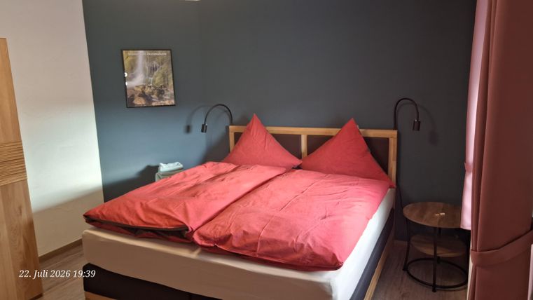 Ein gemütliches Schlafzimmer mit einem großen Bett und roten Kissen. An der Wand hängt ein Bild, und es gibt einen kleinen Tisch daneben.
