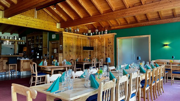 Rustikales Restaurant mit Holzmöbeln, gedeckten Tischen und grünen Servietten. Holzdecke und grüne Wände schaffen eine gemütliche Atmosphäre.