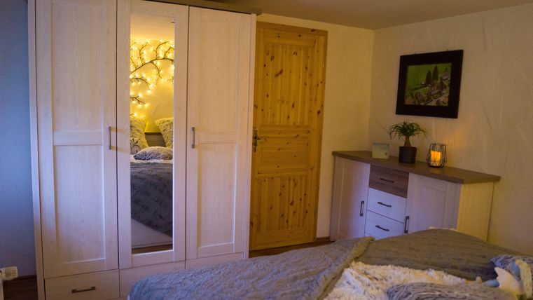 Een gezellige slaapkamer met een witte kast en een houten deur. De sfeer wordt verlicht door lichtjes en planten in de kamer.