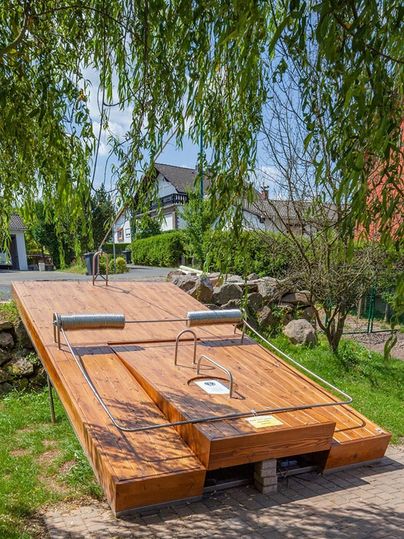 Groot houten platform in de vorm van een muizenval, omringd door bomen en huizen.