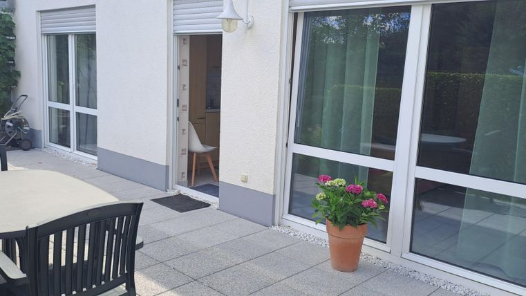 A beautiful outdoor area with a table and chairs. Windows with curtains and some plants create an inviting atmosphere.