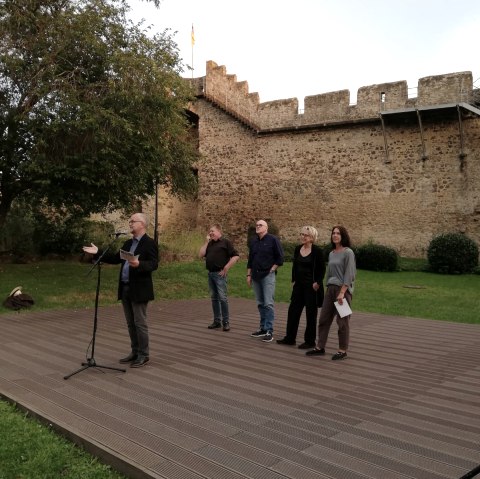 Five people on a flat open-air stage in front of the Hillesheim city wall
