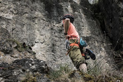 Ein Kletterer mit Helm und Ausrüstung betrachtet eine steile Felswand, bereit zum Aufstieg.