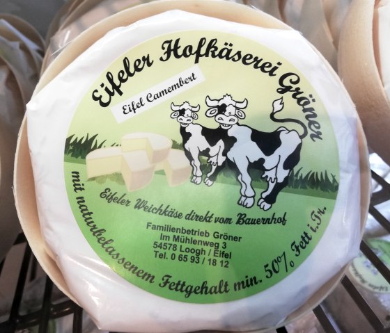 A wheel of Camembert from the Eifeler Hofkäserei Gröner cheese dairy with a photo of two cows on the packaging, the manufacturer's address and information on the fat content.