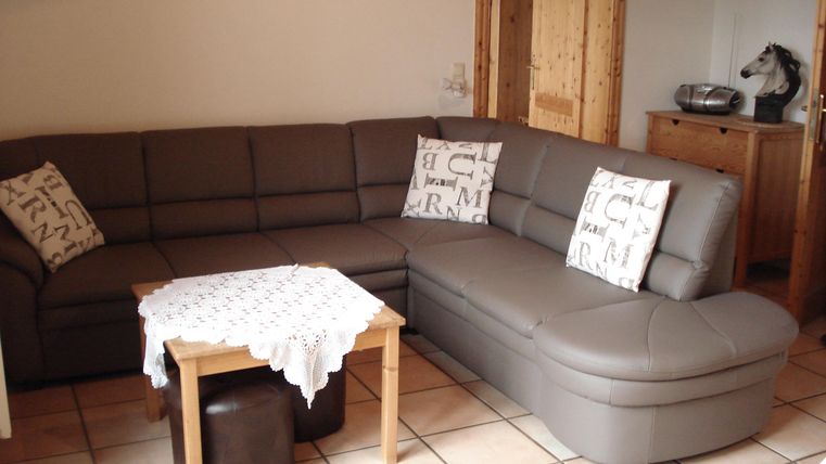 Een gezellige woonkamer situatie met een bruine hoekbank en een kleine houten koffie tafel. Op de bank liggen decoratieve kussens.