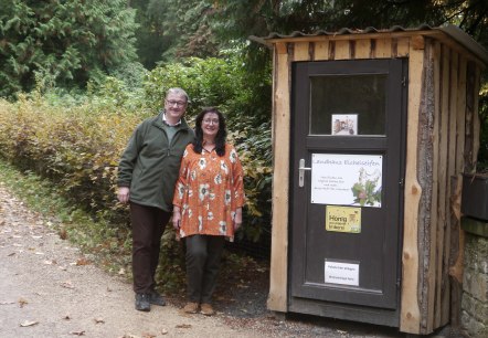 A man and a woman are standing next to a small wooden hut with the words “Landhaus Eichelseifen” written on it.