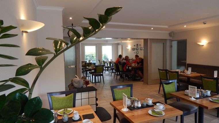 Ein modernes Restaurant mit gedeckten Tischen und einer angenehmen Atmosphäre. Im Hintergrund sind Gäste beim Essen zu sehen.