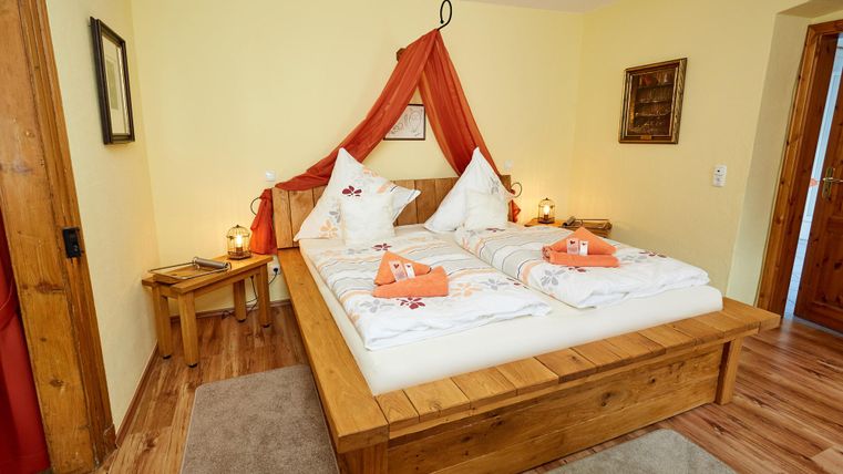 Ein gemütliches Schlafzimmer mit einem großen Bett aus Holz. Sanfte Farben und dekorative Elemente sorgen für eine einladende Atmosphäre.