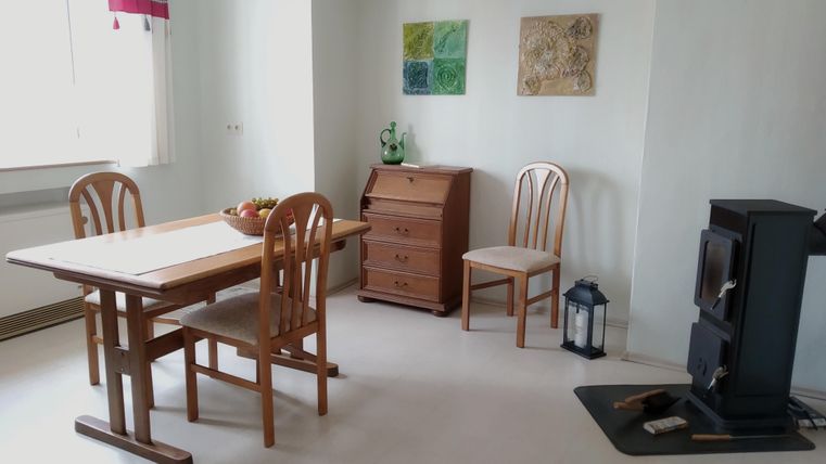 Un appartement confortable avec une table à manger et deux chaises. Des tableaux sont accrochés au mur et un poêle se trouve dans le coin.