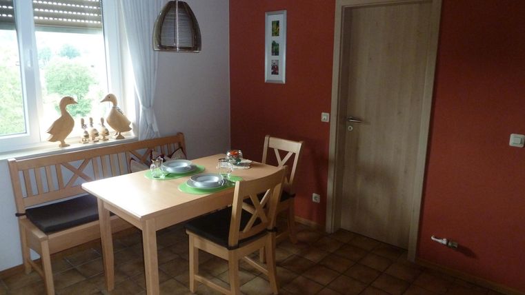 A cozy dining area with a wooden table and two chairs. The walls are partly painted red, and a window provides light.
