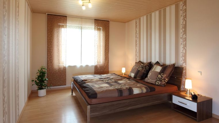 Ein helles Schlafzimmer mit einem großen Bett und gemütlichen Kissen. Die Wände sind mit modernen Mustern dekoriert und ein Fenster sorgt für viel Tageslicht.