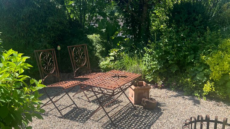 Un jardin confortable avec une petite table et deux chaises. Entouré de verdure luxuriante et de lumière du soleil éclatante.