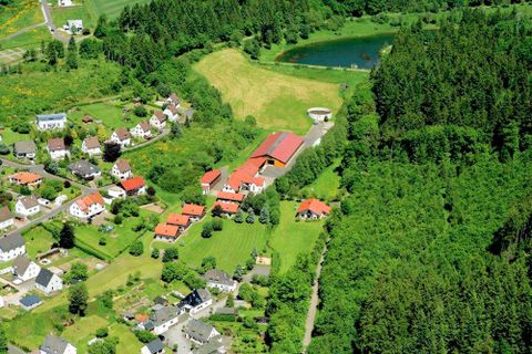 Vogelperspektive auf einen Ferienhof mit mehreren roten Gebäuden am Waldrand, umgeben von Feldern