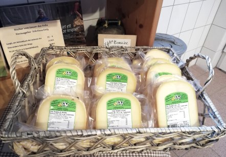 A wooden basket filled with several shrink-wrapped pieces of cheese from the Gr&ouml;ner Hof brand.