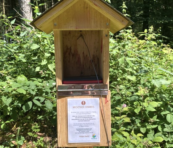 An open wooden house with an information sign and a stamp hanging from a wire rope.