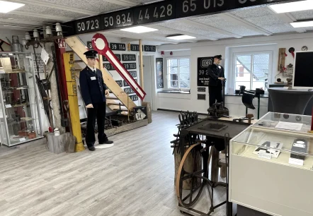 Ausstellungsraum eines Museums zum Thema Eisenbahngeschichte mit Puppen in Schaffneruniform, Schranken, Plaketten und vieles mehr.