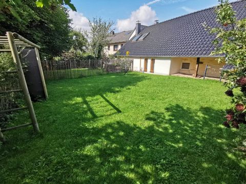 Ein grüner Garten mit frisch gemähtem Rasen und einigen Bäumen. Im Hintergrund sind ein Haus mit einem schrägen Dach und ein Spielgerät zu sehen.