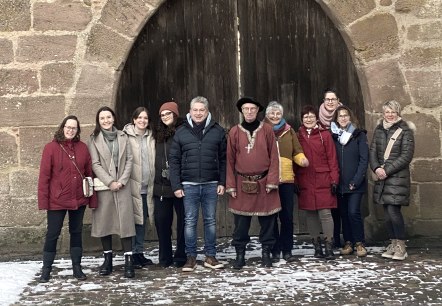 Elf personen staan voor een grote poortboog van de Bertradaburg in Mürlenbach. Een van de personen is gekleed als een middeleeuwse schildknaap.